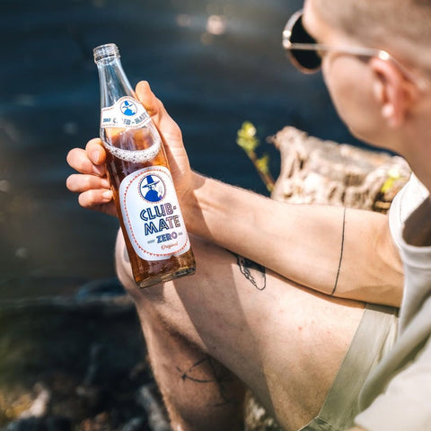 man holding a bottle of club mate zero by the water