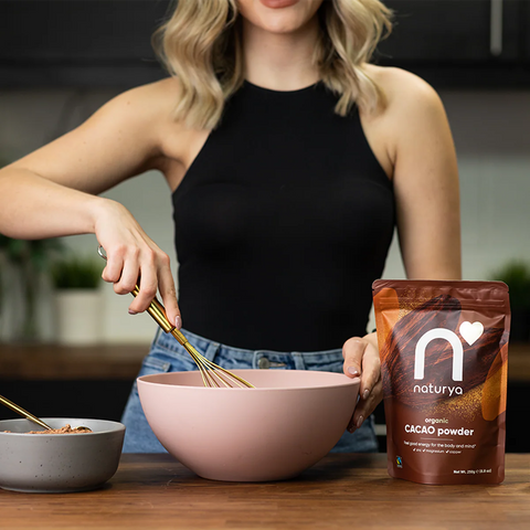 woman mixing with a whisk in a bowl next to a bag of cacao powder on wooden surface