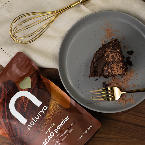 cocoa powder next to a plate with chocolate dessert and a whisk on wooden surface