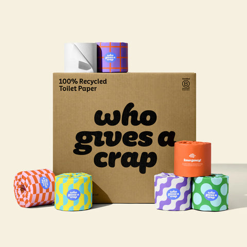 Box of 'who gives a crap' recycled toilet paper with various colored rolls around it.