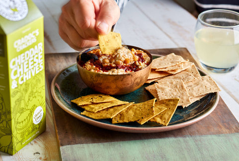 Dipping cracker into a bowl of dip on a plate with a box of crackers and glass of water.