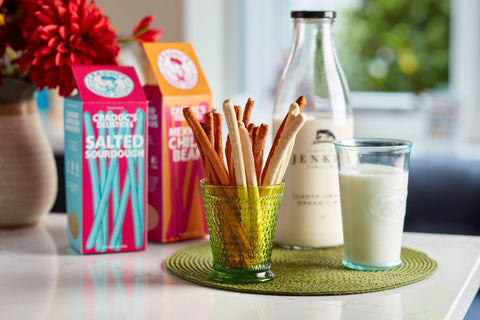 Biscuit sticks in a glass with milk, boxes of cookies, and a bottle on a table.
