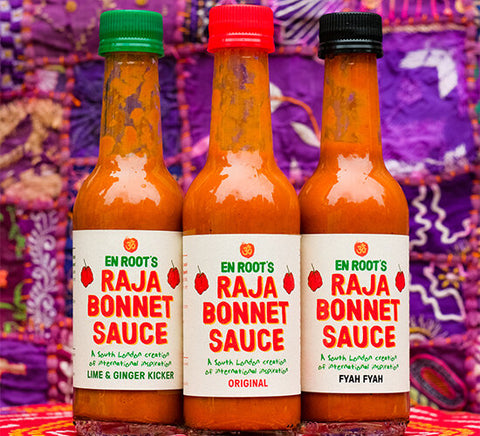 three bottles of different flavors of raja bonnet sauce in front of purple colorful fabric