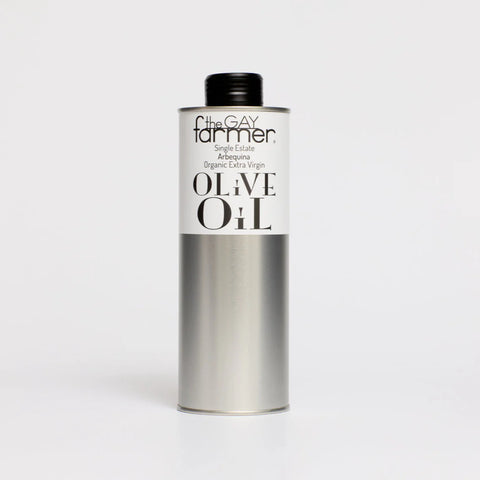 A silver cylindrical bottle of The Gay Farmer Organic Extra Virgin Olive Oil with a black cap and white label, set against a plain light gray background.