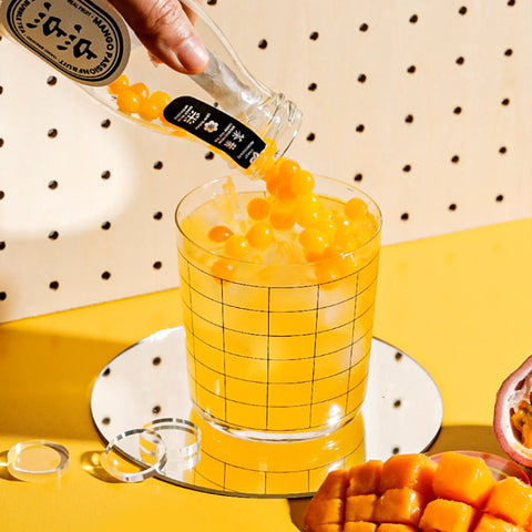 Person pouring a bottle of tea into a glass with ice cubes on a yellow background.