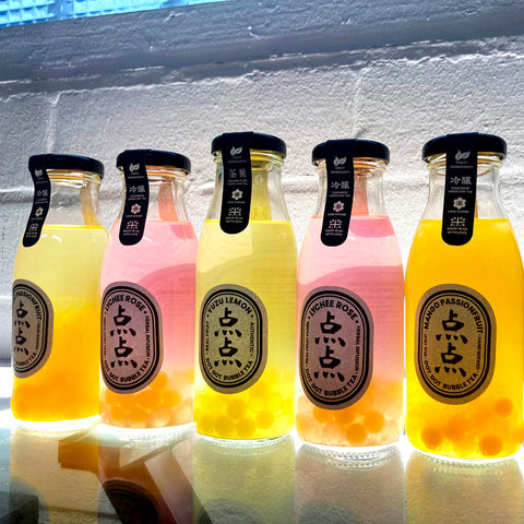 Five bottles of bubble tea with different flavors on a reflective surface.