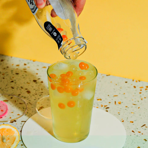 Person pouring a drink from a bottle into a glass with ice and orange slices on a yellow background