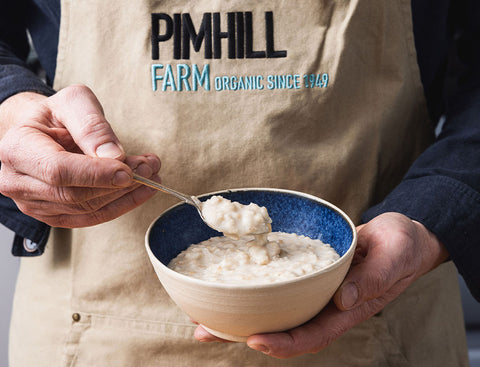 Person holding a bowl of food with a spoon, wearing a Pimhill Farm apron.