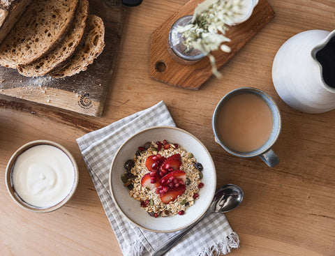 Breakfast scene with oatmeal, fruit, yogurt, and coffee on a wooden table.