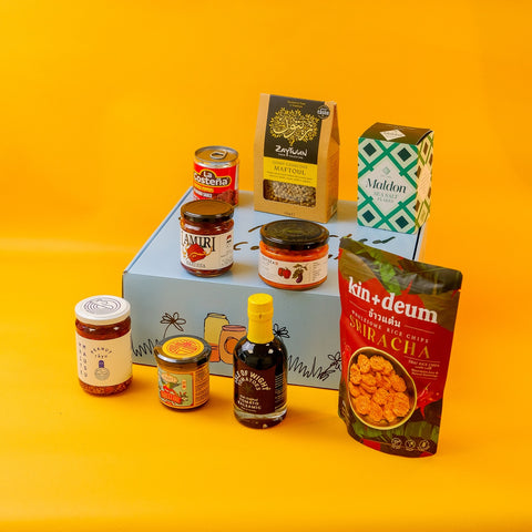 Assorted food products including jars, bottles, and boxes on a hamper box with a yellow background