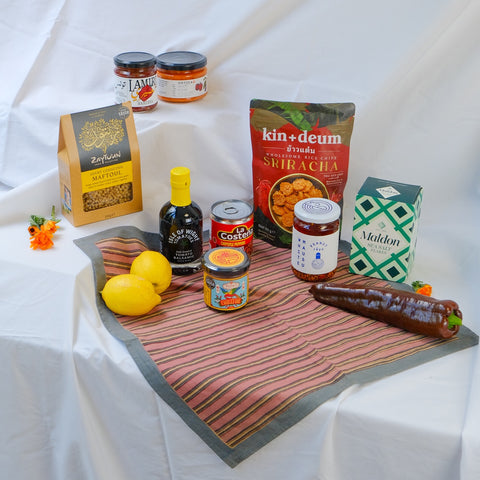 Assorted food products including lemons, a bottle, jars, and packets on a patterned tray with a white background.