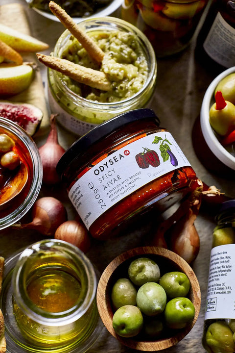 jar of spicy ajvar surrounded by olives, onions, and other food