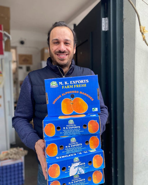 London shop-keeper holding cases of alphonso mangoes