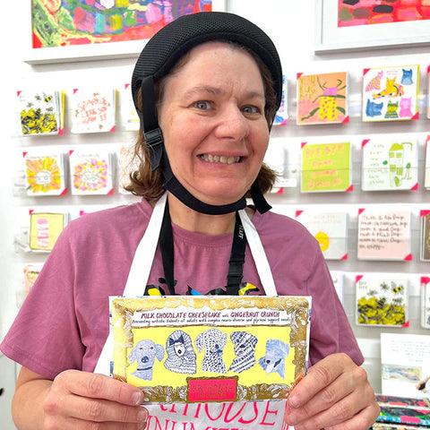 Person holding a chocolate bar with colorful packaging in front of a display of greeting cards.