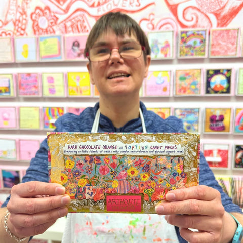 Person holding a chocolate bar with colorful packaging in front of a display of cards.