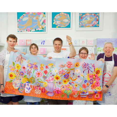 Group of people holding a large colorful artwork in an art studio.