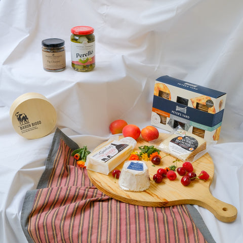 Assorted food items including cheese, fruits, and a charcuterie board on a white fabric background.