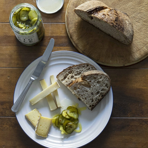 Plated bread, cheese, and pickles on a wooden table