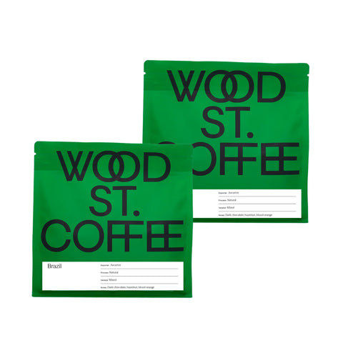 Two green Wood St. Coffee coffee pouches with black lettering and white label areas, shown on a plain white background.