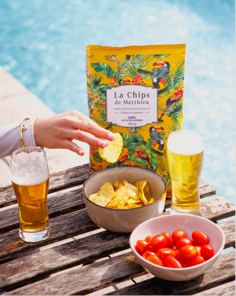 Bag of belsia crisps with beers, tomatoes, and a pool in the background