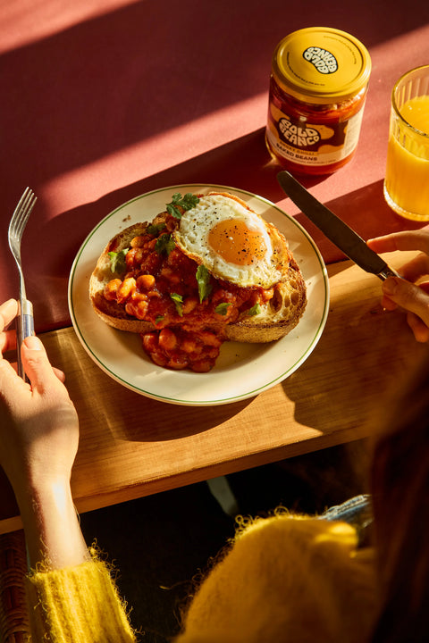Person about to eat a plate of food with a jar of bold bean beans and glass of juice on a wooden table.
