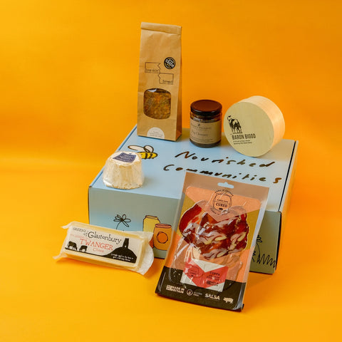 Collection of cheese and charcuterie on a blue hamper box with a yellow background