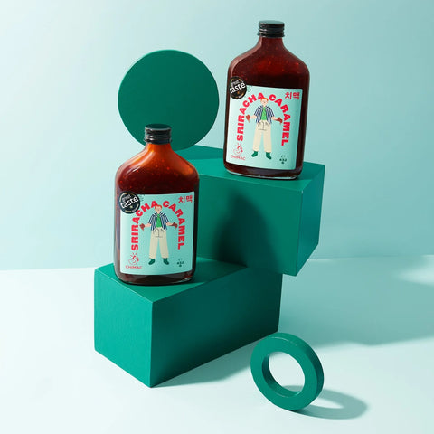 two bottles of sriracha caramel on teal boxes on an ombre teal background