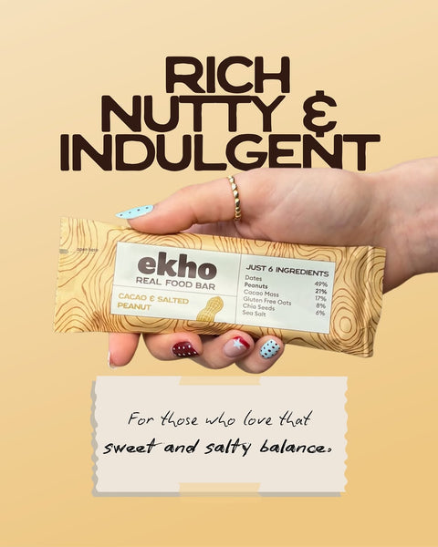 A hand holds an Ekho Real Food Bar in a wood-grain wrapper against a warm beige background with promotional text reading 'RICH NUTTY & INDULGENT' and a note below.