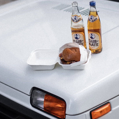 two bottles of club mate on a car with food
