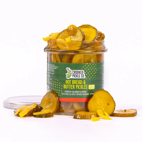 container of hot bread & butter pickles with pickles spilling out on white background