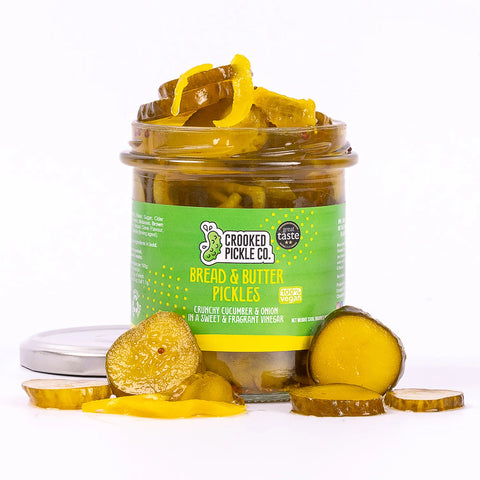 container of bread & butter pickles with pickles spilling out on white background