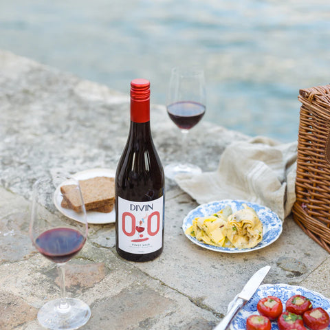 Bottle of Divin O.O wine with glasses and snacks by a waterfront