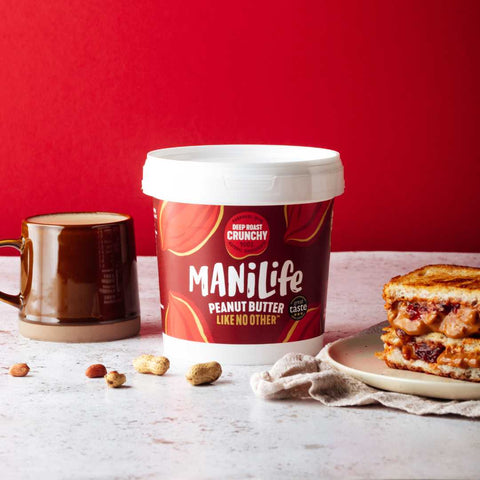 container of peanut butter next to a mug and sandwich on a red background