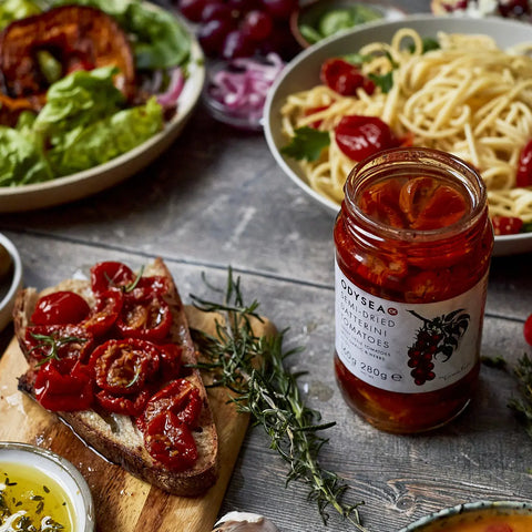 jar of tomatoes next to bread and pasta and salad on wood surface