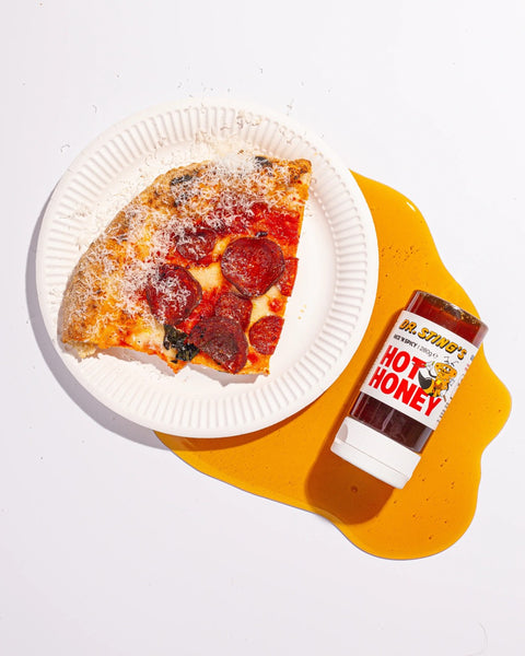 Slice of pepperoni pizza with hot honey bottle next to it