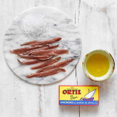 Anchoas ( Anchovies ) on a marble board with a container of olive oil and Ortiz brand packaging.