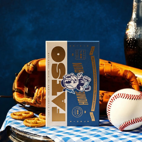FATSO Hot Cocoa box with a baseball, glove, and cookies on a checkered tablecloth.