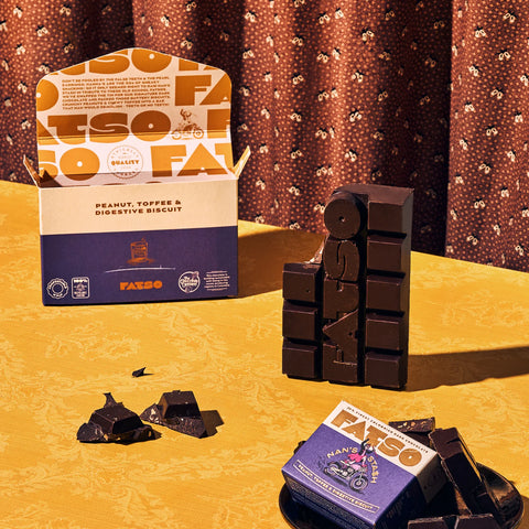 Chocolate bars and packaging on a yellow surface with a patterned curtain background