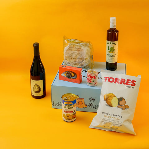 Assorted food items including a bottle of wine, a hamper box, and various packaged foods on an orange background.
