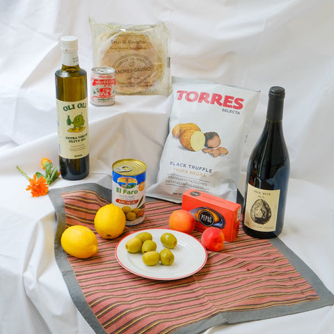 Assorted food items including olive oil, wine, and fruits on a white surface