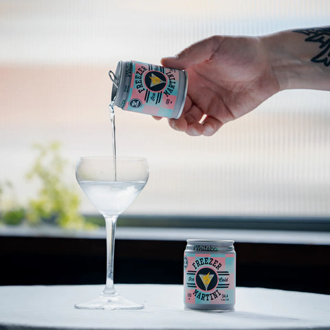 Hand pouring a clear liquid from a can labeled 'Freezer' into a glass on a blurred background.