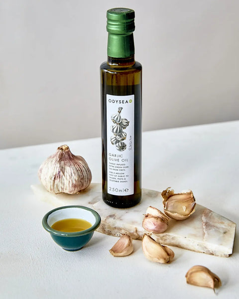 Bottle of Odysea Garlic Olive Oil with garlic bulbs on a white surface