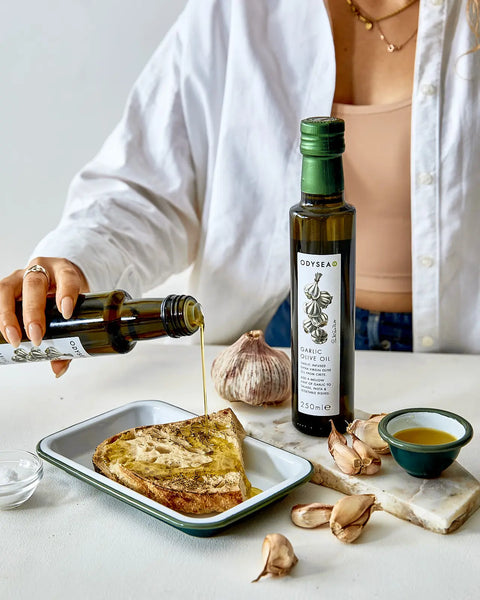 Person pouring olive oil onto toast with a bottle of olive oil in the background