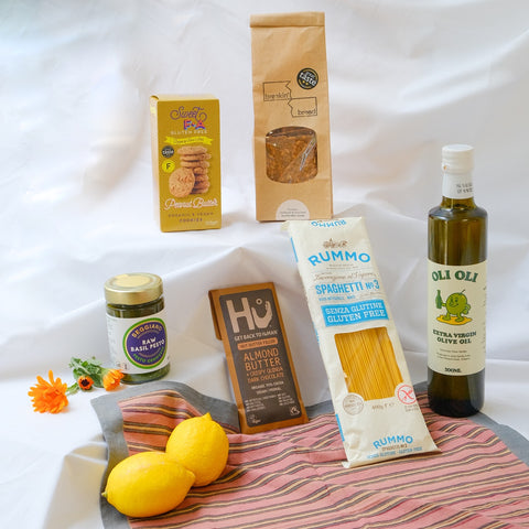 Assorted groceries including GF pasta, olive oil, and lemons on a white background