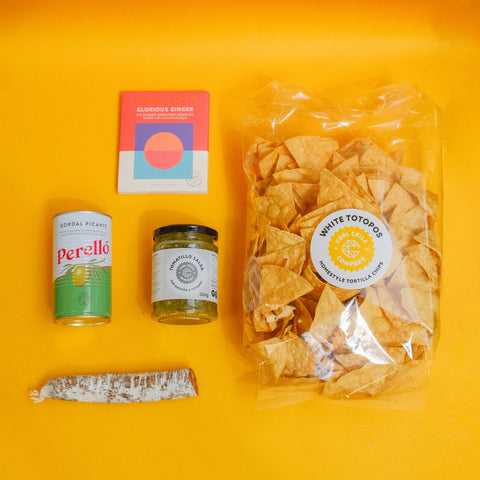 Packaged tortilla chips with a jar, can, and block of cheese on an orange background