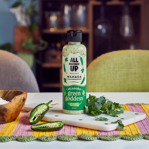 Bottle of All Dressed Up Wahaca Jalapeno Green Goddess dressing on a table with ingredients.