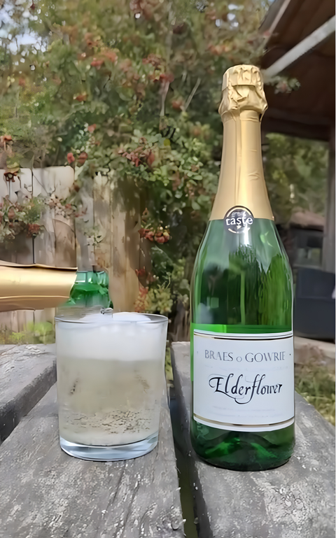 bottle of elderflower cairn o'mohr on a wooden table next to a glass with liquid being poured into it