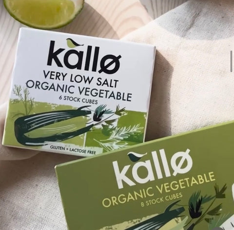 Two boxes of Kallø Organic Vegetable stock cubes on a light fabric surface, with a lime wedge partially visible in the top left corner.