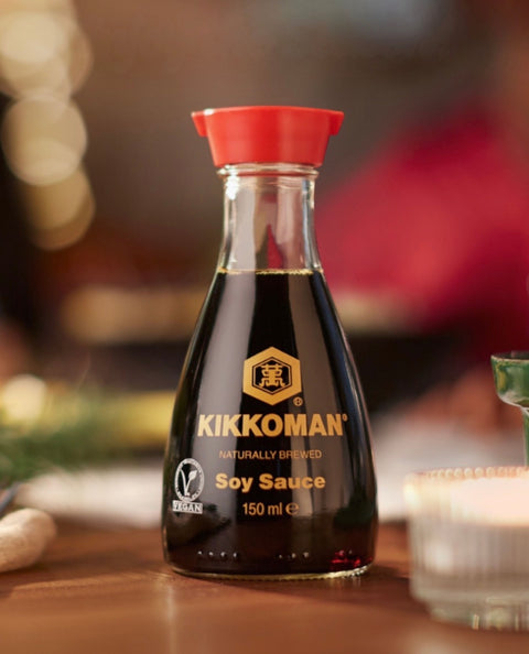 A bottle of Kikkoman soy sauce on a wooden table, with a warm, blurred background.