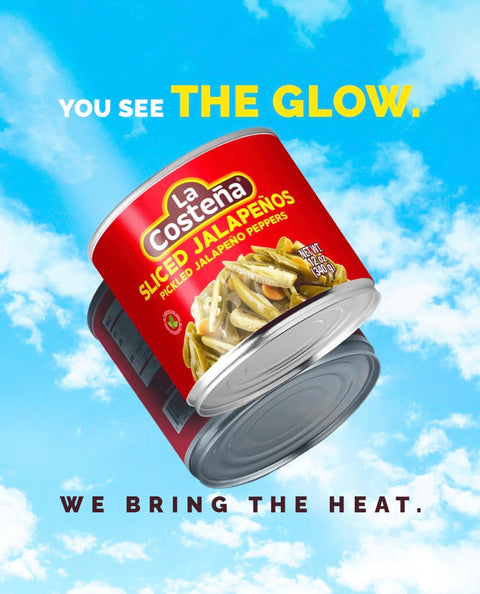 A can of La Costena Sliced Jalapeños floating against a blue sky with clouds. The can is red with yellow and white branding, and the food photo shows sliced jalapeños.